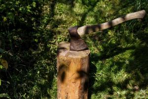 un hacha de hierro con mango de madera clavada en un tocón de pino en el bosque. foto
