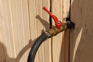 The water tap is sticking out of the wall of the house. Iron water tap with a red handle. photo