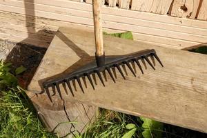 A black rake stands on a wooden bench near the wall of the house. photo
