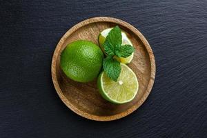 Limes with mint on wooden plate on dark stone background. photo