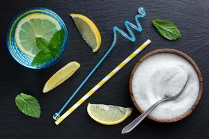 Water with lemon and mint in glass and sugar in wooden bowl on dark stone background. photo