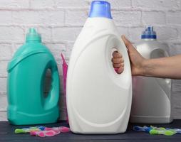 mano de mujer sosteniendo una botella grande de plástico blanco con detergente para lavar ropa