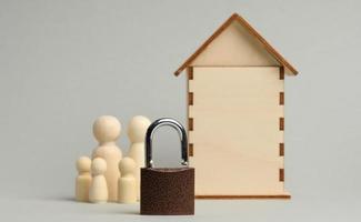 metal padlock on the background of a wooden miniature house and wooden figures of a family on a gray background. photo