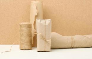 box, roll of brown kraft paper and reel with brown rope on white table, packing material photo