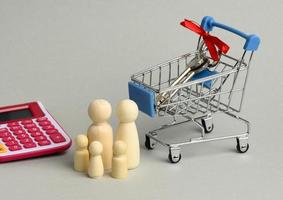 family of wooden figures and metal keys in a miniature pink trolley on a gray background. real estate purchase concept photo