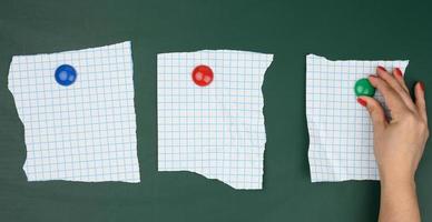 female hand attaches blank sheets of paper in a cage to a green magnetic board photo