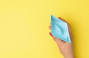 female hand hold a blue paper boat on a yellow background photo