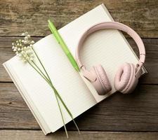 bouquet of blooming lilies of the valley and wireless headphones and a open notepad on a wooden background photo