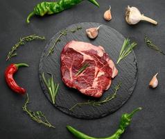 raw piece of beef ribeye with rosemary, thyme on a black table, top view photo