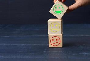 bloques de madera con diferentes emociones, desde la sonrisa hasta la tristeza y la mano de una mujer. concepto para evaluar la calidad de un producto o servicio foto