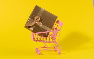 brown gift box with a silk bow in a miniature metal trolley on a yellow background photo