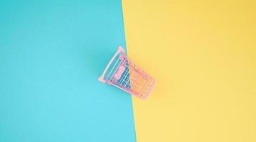 pink empty miniature metal shopping cart on a blue yellow background photo