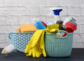 sponges, plastic brushes and bottles of detergents on a blue wooden table. Household cleaning items on white brick wall background photo