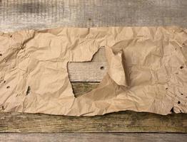 hoja rota de papel marrón con un agujero en un fondo de madera de tablas foto