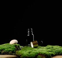 botella de vidrio negro con soportes de pipeta sobre musgo verde, fondo negro. marca de spa de cosméticos. embalaje para gel, suero, publicidad y promoción de productos, maqueta foto