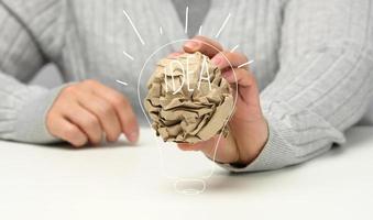 la mano femenina sostiene una bola de papel marrón arrugada. nueva idea, lluvia de ideas foto