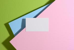 blank rectangular business card lies on a modern bright green background with blue and pink sheets of paper with a shadow photo