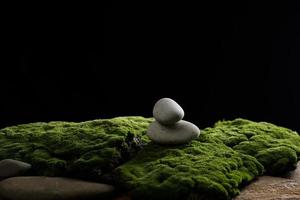 stack of round stones on green moss, black background. Podium to showcase products, cosmetics and items, advertising photo