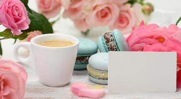 tarjeta de visita blanca en blanco y taza con café espresso y taza de cerámica blanca con café y macaron azul sobre una mesa blanca, foto