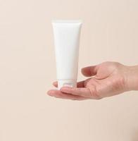 la mano femenina sostiene tubos de plástico blancos vacíos para cosméticos. embalaje para crema, gel, suero, publicidad y promoción de productos, maqueta foto