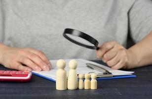 wooden figurines of little men family on the background of a man with a magnifying glass, who will examine the documents. photo