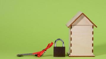 miniature wooden house and metal lock on a green background, security concept photo