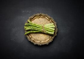 Fresh green asparagus sprouts on a round copper plate, black background. photo