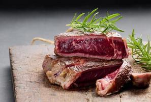 fried piece of beef ribeye, cut into pieces on a brown wooden board, rare doneness photo