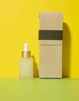 White glass transparent bottle with a pipette for cosmetics, oils, acids on a white table. Yellow background photo