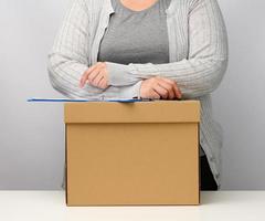 A woman in gray clothes stands near a brown box. The concept of moving, sending and receiving goods. Dismissal from work photo