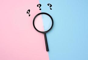 black magnifier on a pink-blue background and question marks. The concept of uncertainty and the search for solutions, doubts photo
