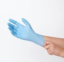 proceso de poner guantes de látex azules a mano sobre fondo blanco, protector de higiene foto