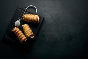 baked tubules filled with whipped egg white cream on a black wooden kitchen board, top view photo