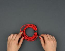 female hand holds twisted cable for charging mobile devices in a red textile wrapper on a black background photo