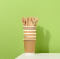 brown paper cardboard cups and wooden stirring sticks on a white table, green background. photo