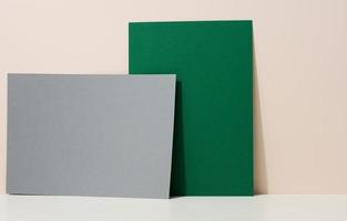 blank green and gray cardboard sheet of paper with shadow on white table. Template for flyer, announcement photo