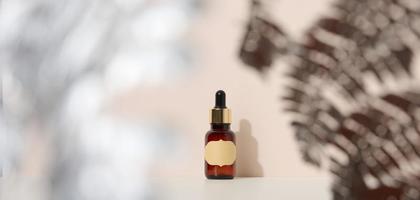 brown glass bottle with a pipette stands on a brown background. Container for cosmetics, serum and oil, silver fern leaf photo