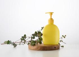 yellow plastic container with a dispenser on a wooden background and a branch of eucalyptus on a white background. Container for liquid soap, shampoo photo