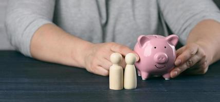 wooden figurines of little men family on the background of a man with a piggy bank photo