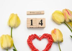 yellow tulips, wooden calendar with date 14 February and red heart on white background photo