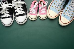 muchas zapatillas textiles multicolores y gastadas de diferentes tamaños sobre un fondo verde foto