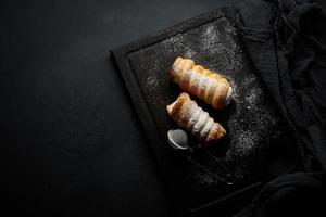 baked tubules filled with whipped egg white cream on a black wooden kitchen board, top view photo