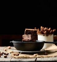 pieces of baked brownie in a metal black frying pan on the table photo