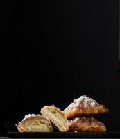 Stack of baked croissants sprinkled with powdered sugar on a black background photo