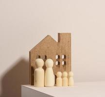 figuras familiares de madera, casa modelo sobre un fondo beige. compra de bienes raíces, concepto de alquiler. mudarse a nuevos apartamentos foto