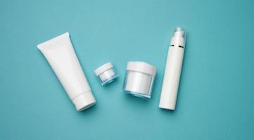 jar, bottle and empty white plastic tubes for cosmetics on a blue background. Packaging for cream, gel, serum, advertising and product promotion photo