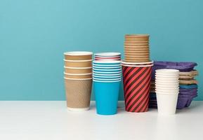 stack of paper disposable multi-colored cups and stand on white table, blue background photo