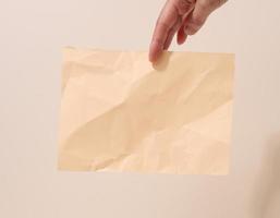 la mano femenina sostiene una hoja de papel arrugada sobre un fondo beige. lugar para inscripciones y anuncios foto