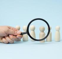 wooden figures of men stand on a blue background and a black magnifying glass photo