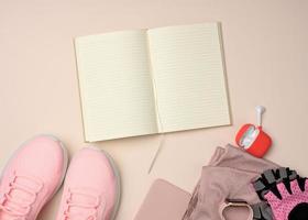 open notebook with blank pages, pink sneakers and smart gadgets on a beige background. Place to record goals and achievements, schedule photo